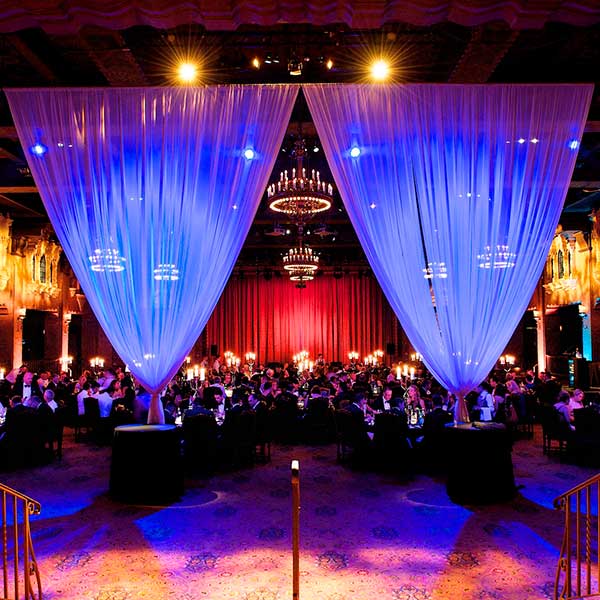 A room of people at a dark, candle lit event, with a red curtain behind the main stage and purple-lit drapes in the foreground